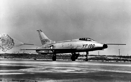Black-and-white HD PC desktop wallpaper/background of a military North American F-100 Super Sabre on a runway, drogue parachute deployed, YF-100 markings visible.