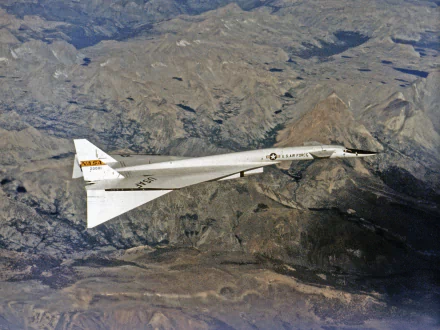 Military North American XB-70 Valkyrie supersonic prototype flying over rugged mountains — 2K Quad HD PC desktop wallpaper/background.
