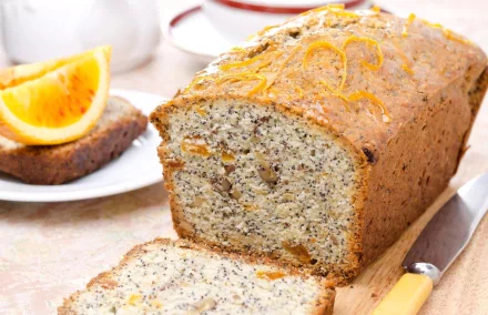 A close-up of a freshly baked bread loaf, featuring a textured surface and poppy seeds, with slices displayed alongside orange slices. This HD image serves as an appealing desktop wallpaper.