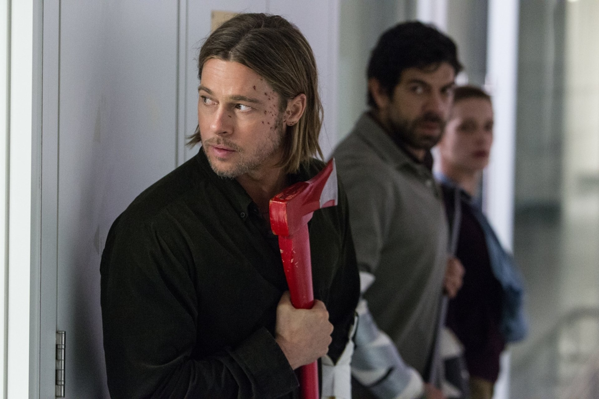 HD desktop wallpaper from the movie World War Z, showing a tense scene with Brad Pitt holding a red axe, with two men standing behind him in a corridor.
