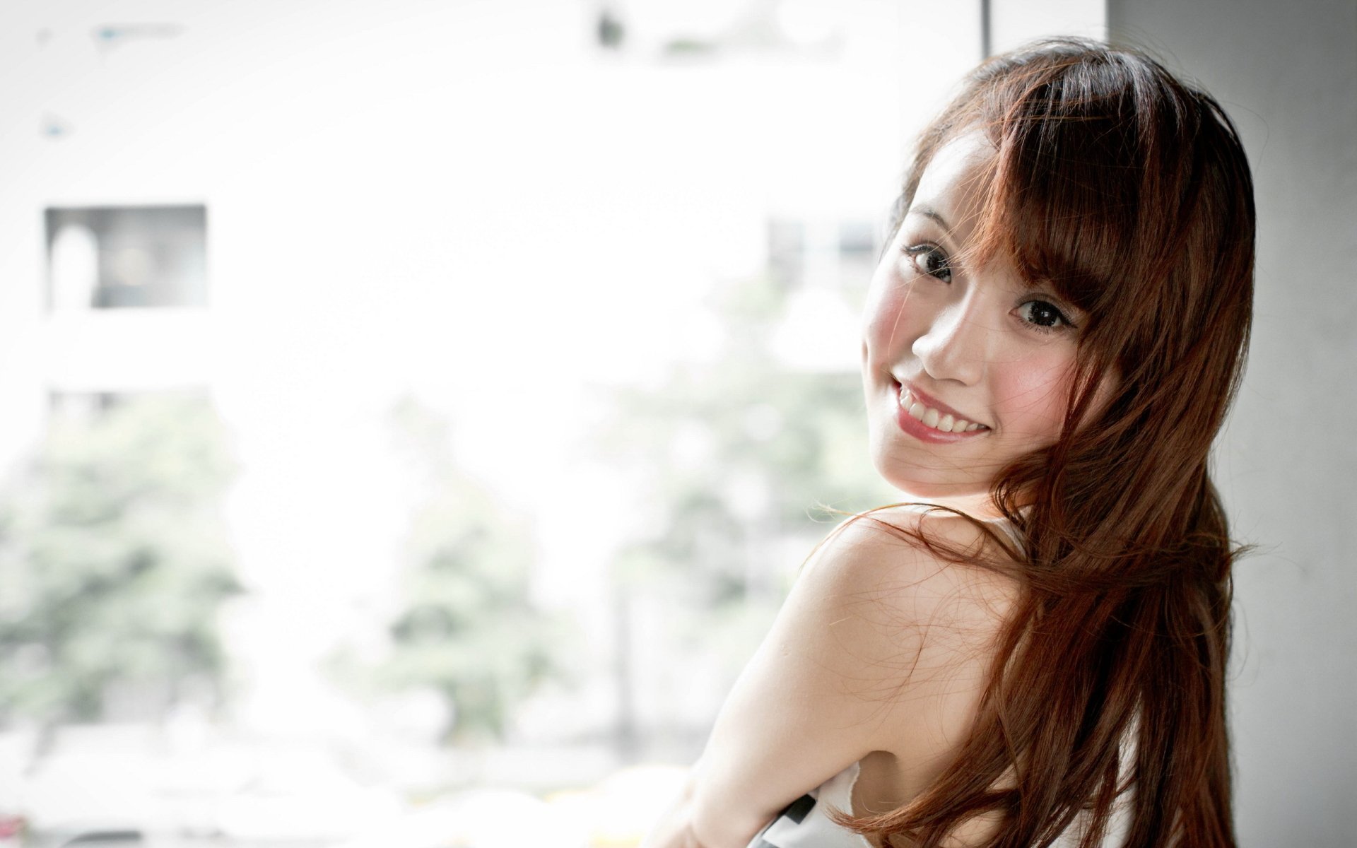 A smiling woman with long hair poses near a window, exuding a positive mood. This HD image serves as an engaging desktop wallpaper or background.