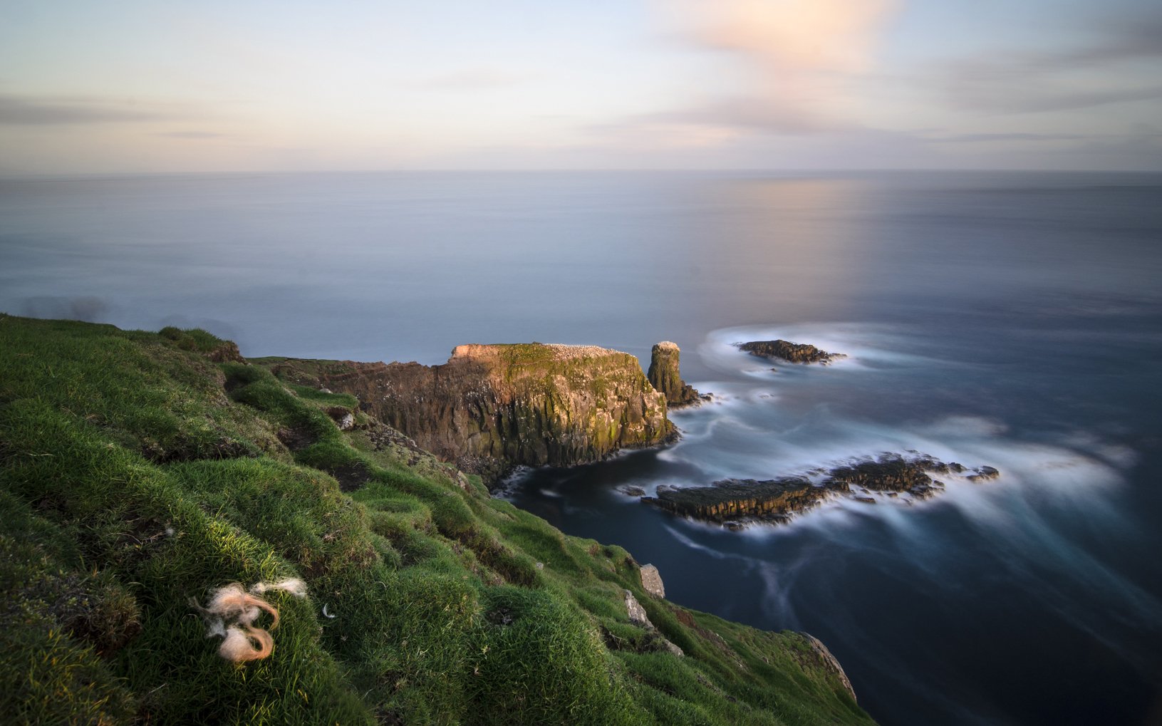 HD PC desktop wallpaper and background — nature coastline: grassy cliff overlooking rocky islets and a silky long-exposure sea beneath a pastel sky.