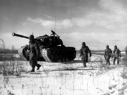 Black-and-white Korean War scene: soldiers walking past a tank across a snowy field — military 2K Quad HD PC desktop wallpaper and background.