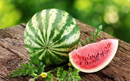 HD PC desktop wallpaper showing a whole watermelon and a juicy slice resting on a rustic wooden surface with green foliage and a blurred natural background.