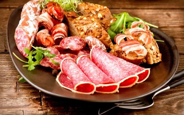 HD desktop wallpaper featuring a plate of assorted cured meats and sliced bread garnished with fresh greens on a rustic wooden table.