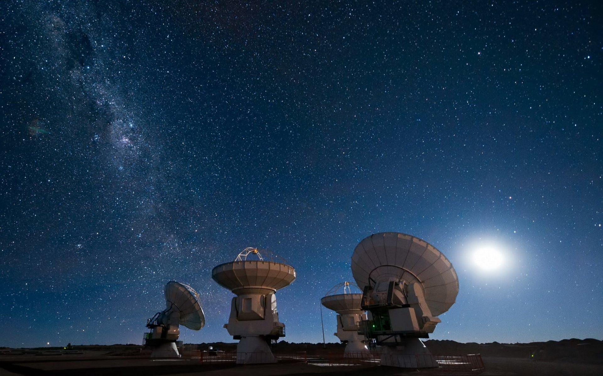 2K Quad HD desktop wallpaper: Milky Way, moon and stars above an array of man-made radio telescopes/radar dishes aimed at the galaxy.