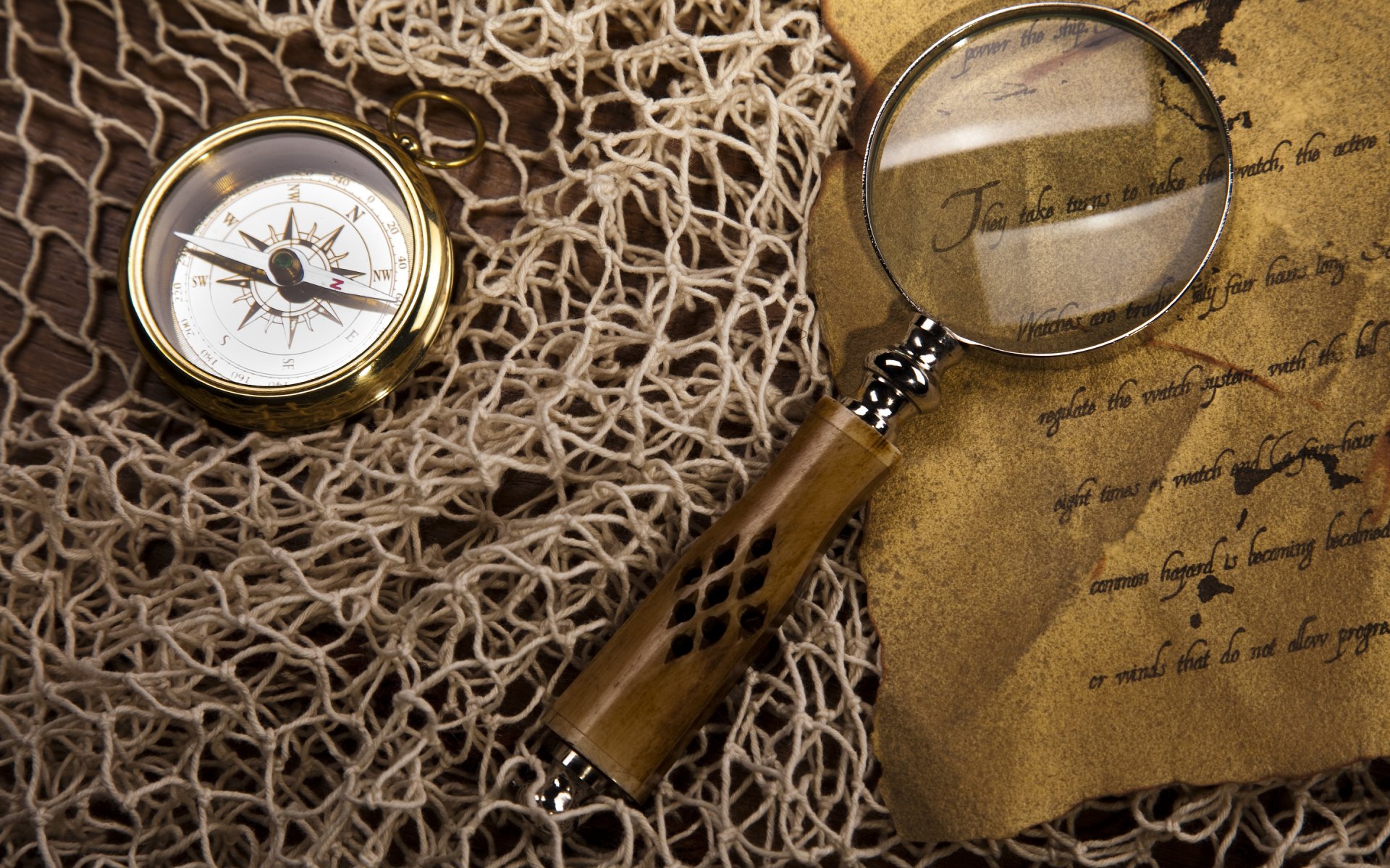 HD PC desktop wallpaper showing a vintage compass, magnifying glass, and an old map or parchment on a textured net background, evoking exploration and discovery.