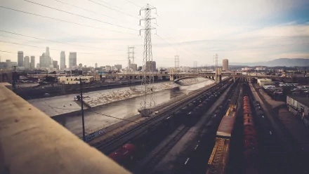 A view of the Los Angeles River alongside railway tracks, featuring the city skyline and power lines in the background, captured in a striking HD image.