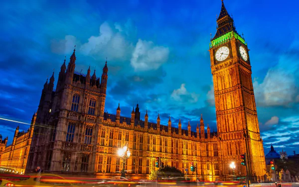 A stunning HD desktop wallpaper showcasing Big Ben illuminated at night, with the historic Houses of Parliament in the background against a vibrant blue sky.
