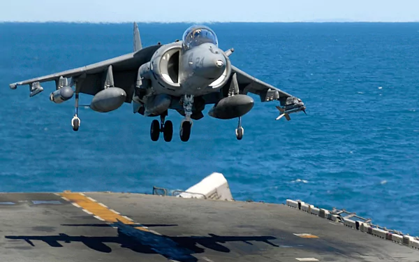 HD desktop wallpaper showing a McDonnell Douglas AV-8B Harrier II military jet taking off from an aircraft carrier over the ocean.