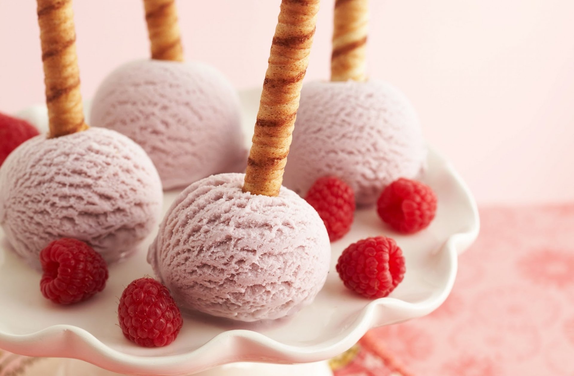 A delightful display of purple ice cream scoops, each perched on a crispy stick, surrounded by fresh raspberries. This HD image serves as a vibrant desktop wallpaper.
