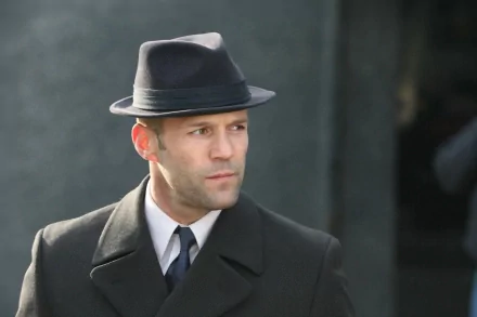 A stylish HD desktop wallpaper featuring Jason Statham in a classic black suit and fedora, exuding charisma and confidence in a cinematic setting.