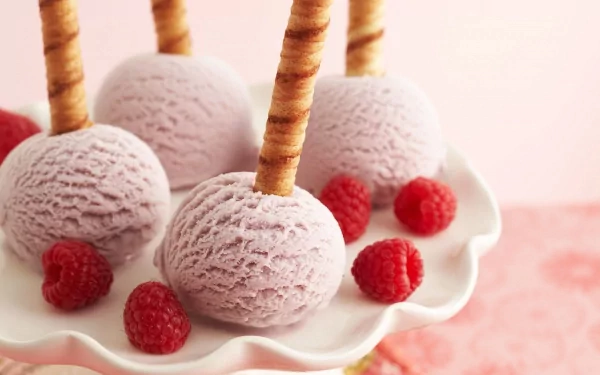 A delightful display of purple ice cream scoops, each perched on a crispy stick, surrounded by fresh raspberries. This HD image serves as a vibrant desktop wallpaper.