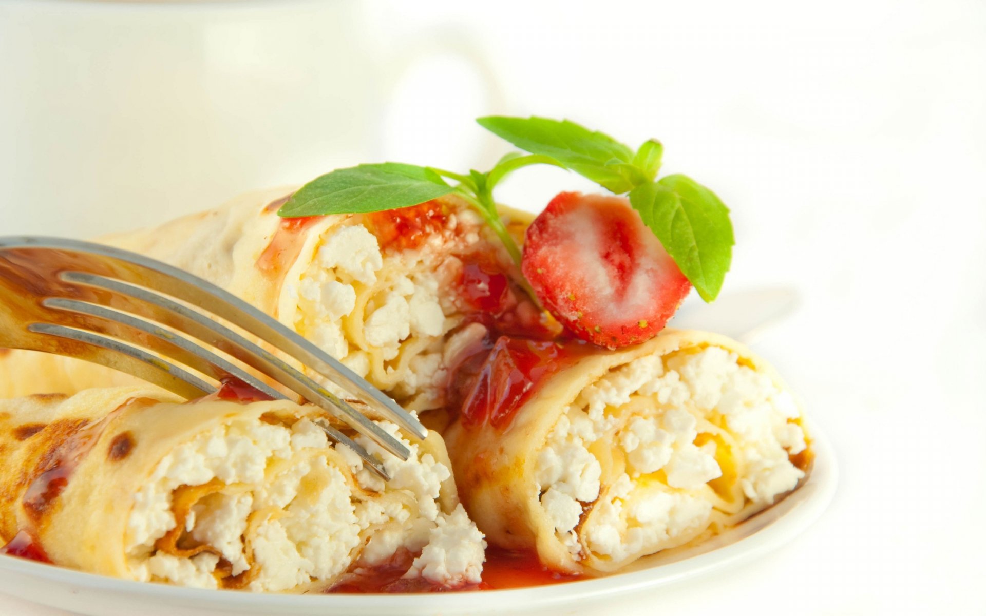 HD PC desktop wallpaper featuring close-up of rolled pancakes topped with strawberry sauce and fresh basil on a white plate with a fork.