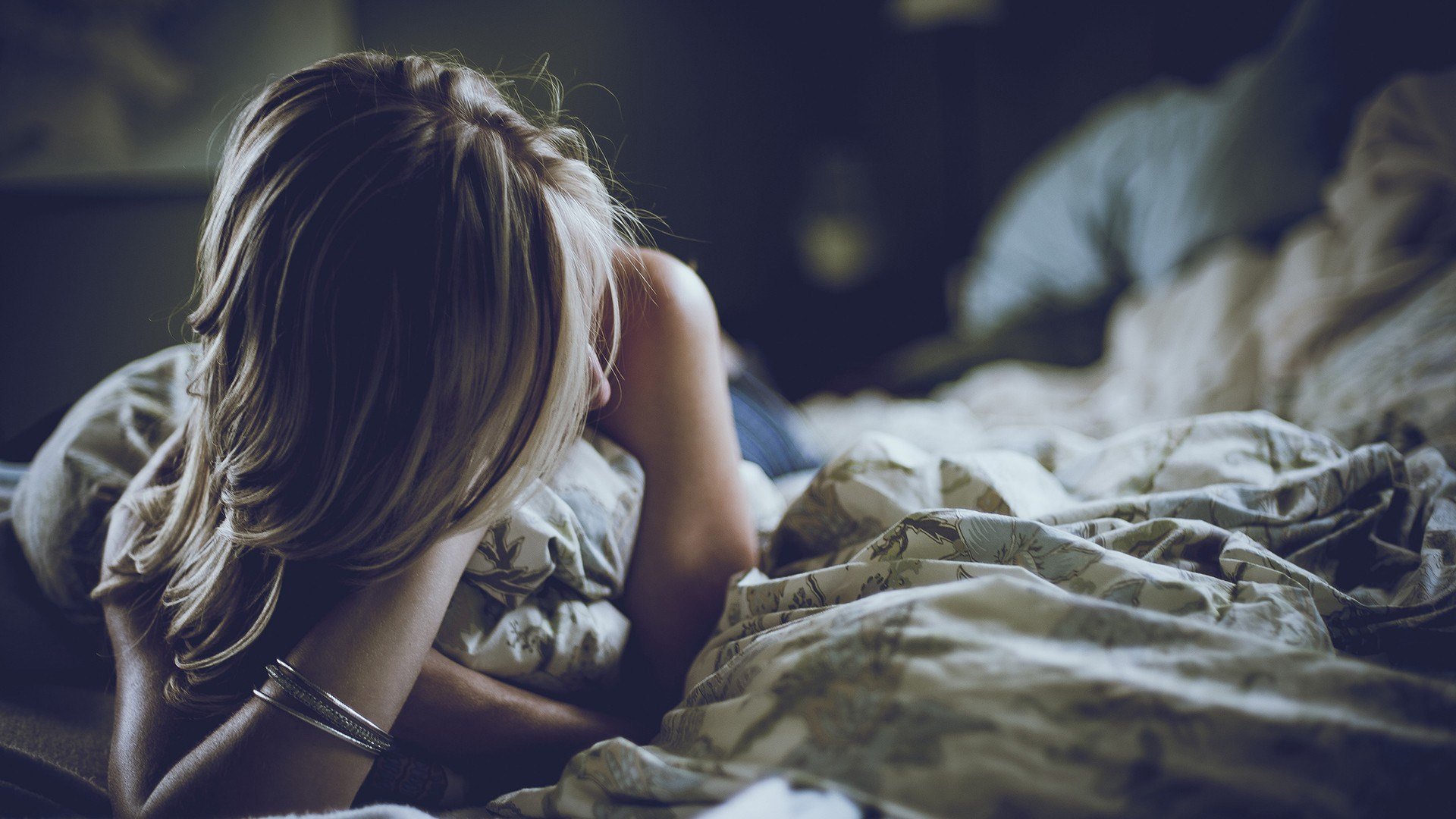 A woman model is seen relaxing on a bed, partially draped in a blanket. The soft lighting creates a serene atmosphere, making this an engaging HD PC desktop wallpaper.
