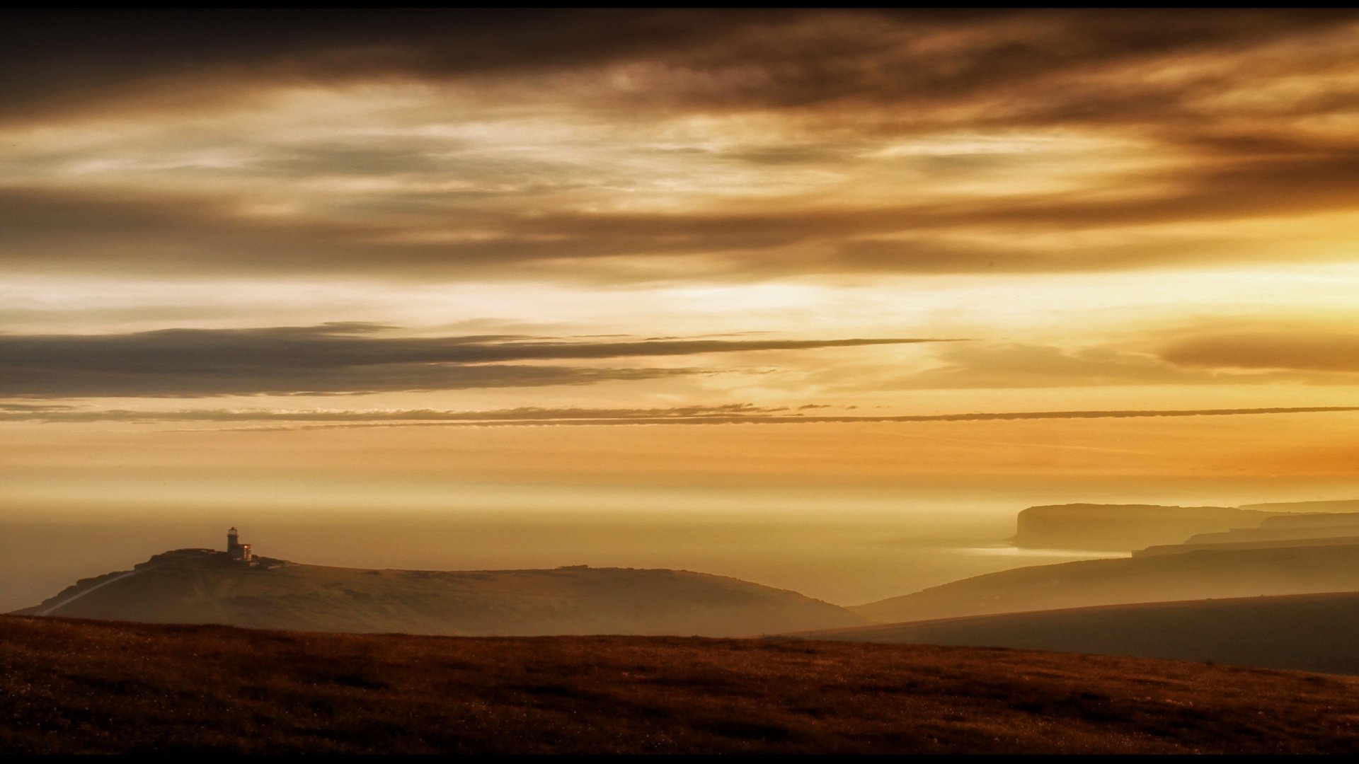 A breathtaking sunset over rolling hills and the sea, showcasing nature's beauty. This HD image serves as a stunning desktop wallpaper and background.