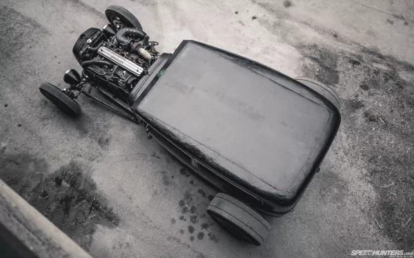 Black rat rod vehicle with exposed engine and minimal bodywork shown from a high angle, set on a textured concrete surface as an HD PC desktop wallpaper.