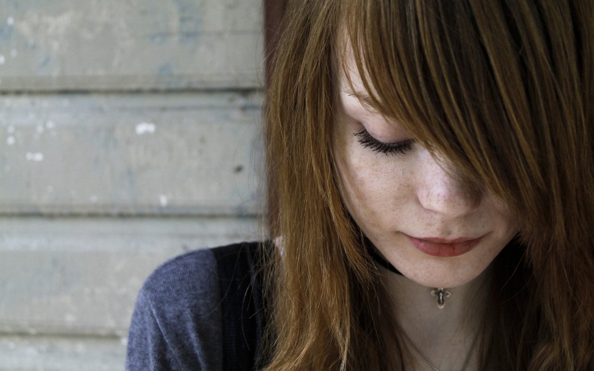 A woman with long, dark blonde hair looks down thoughtfully, set against a rustic background, making for a striking HD desktop wallpaper and background.