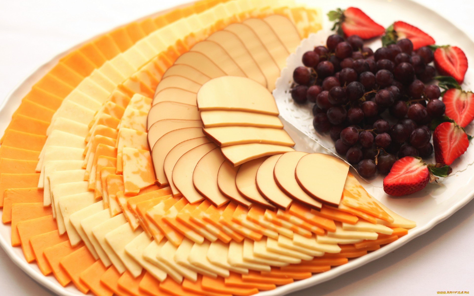 HD desktop wallpaper featuring an appetizing platter of assorted sliced cheeses, red grapes, and fresh strawberries arranged on a white plate.