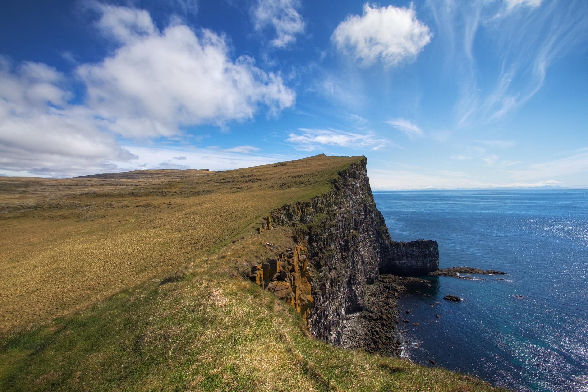 HD PC desktop wallpaper featuring a serene coastline with grassy cliffs under a bright blue sky dotted with clouds, showcasing the beauty of nature.