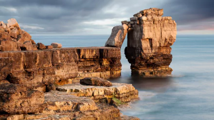 HD desktop wallpaper showcasing a dramatic cliff formation extending into calm ocean waters under a cloudy sky, highlighting natural coastal beauty.