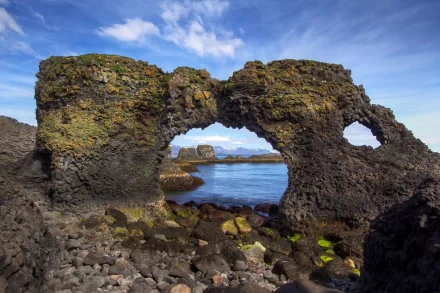 HD nature desktop wallpaper showcasing a rugged cliff formation with natural arches against a blue sky and calm sea background.