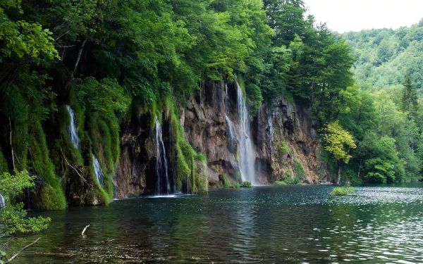 HD PC desktop wallpaper featuring a serene nature scene with lush greenery and multiple waterfalls cascading into a calm lake.