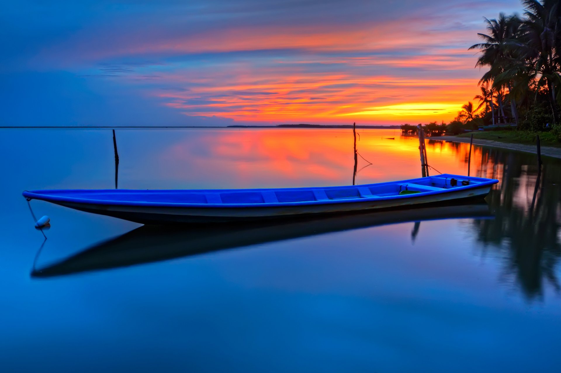 A serene boat rests on still waters at sunset, reflecting vibrant colors in the sky, creating a stunning HD wallpaper for desktop backgrounds.