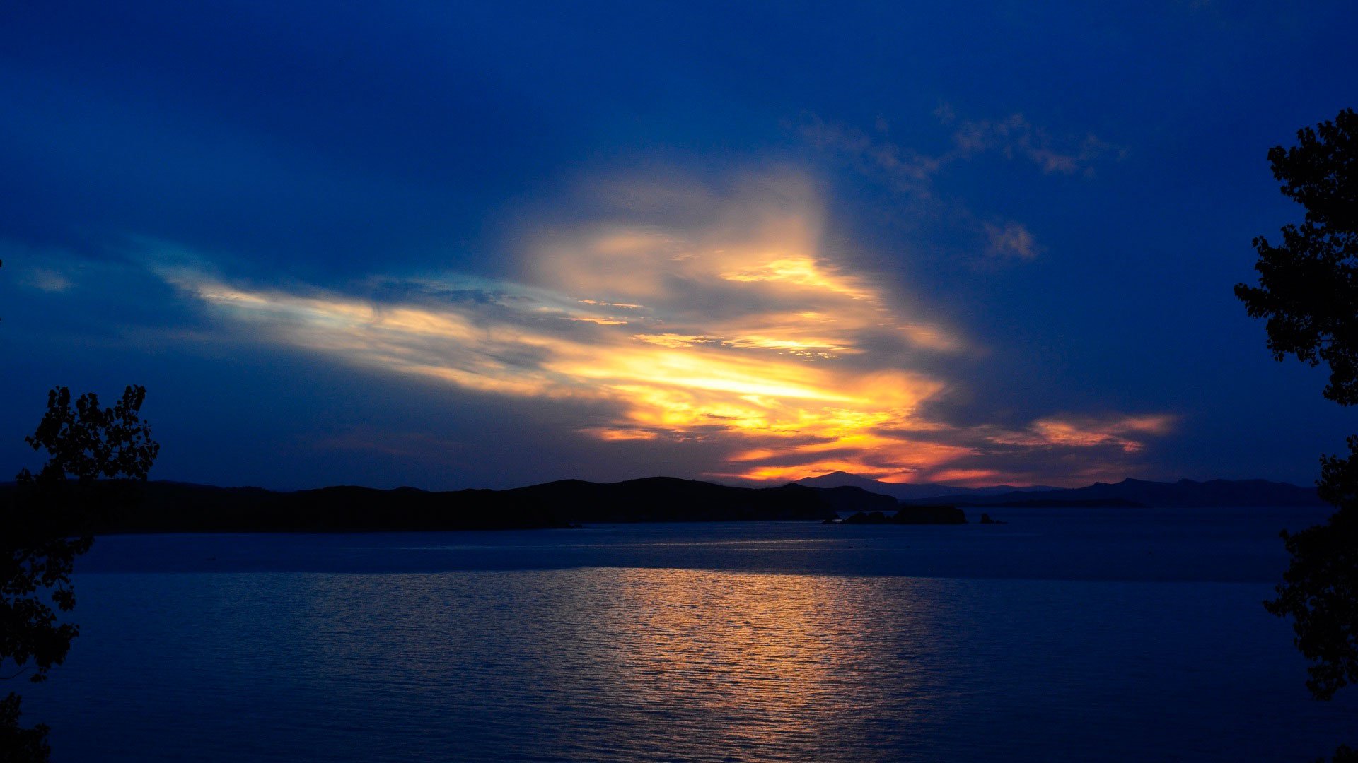 A tranquil sunset over water, featuring deep blues and warm orange hues, creating a serene atmosphere. This HD wallpaper captures the beauty of nature's evening light.