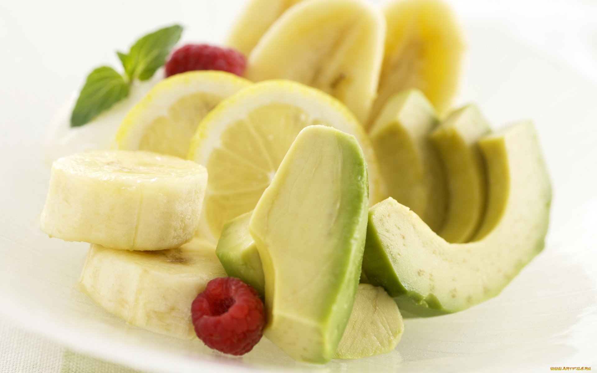 HD PC desktop wallpaper featuring a close-up of sliced banana, avocado, lemon, and raspberries on a white plate, highlighting fresh fruit and food.