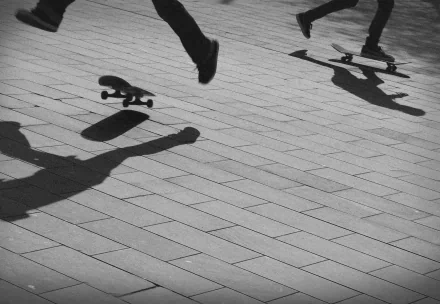 Black and white 4K Ultra HD image capturing dynamic skateboarding action with shadows in motion on a tiled surface, emphasizing sports and movement.