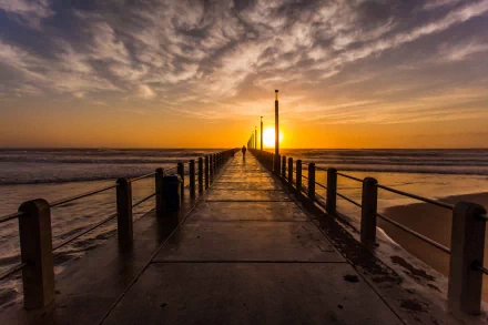 A stunning HD desktop wallpaper featuring a wooden pier extending into the ocean at sunset, with dramatic clouds and warm hues illuminating the scene.