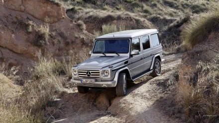 HD PC desktop wallpaper featuring a silver Mercedes-AMG G 63 navigating a rugged, rocky off-road trail in a natural, arid landscape.