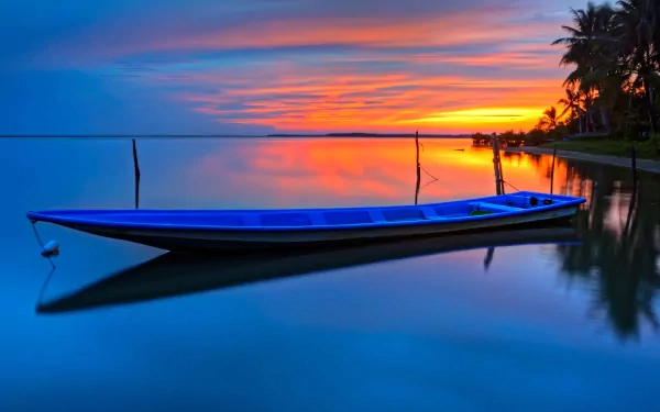 A serene boat rests on still waters at sunset, reflecting vibrant colors in the sky, creating a stunning HD wallpaper for desktop backgrounds.