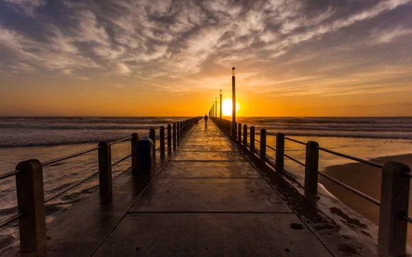 A stunning HD desktop wallpaper featuring a wooden pier extending into the ocean at sunset, with dramatic clouds and warm hues illuminating the scene.