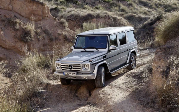 HD PC desktop wallpaper featuring a silver Mercedes-AMG G 63 navigating a rugged, rocky off-road trail in a natural, arid landscape.