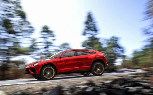 A striking red Lamborghini Urus speeding along a road, set against a blurred backdrop of trees, captured in high-definition for an impressive desktop wallpaper.