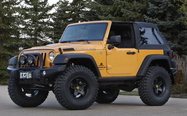 HD PC desktop wallpaper of a yellow Jeep Wrangler Rubicon off-road vehicle parked before trees, black soft top, large tires and front winch.