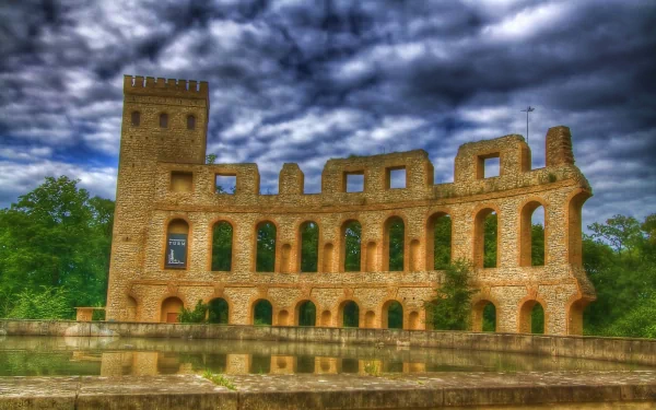 4K Ultra HD PC desktop wallpaper of a stone stadium-like ruin reflected in calm water beneath dramatic storm clouds, framed by lush green trees.