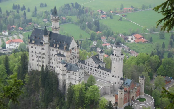 A stunning HD PC desktop wallpaper showcasing the man-made Neuschwanstein Castle nestled among lush greenery and village houses.