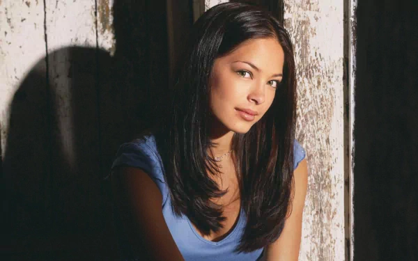 A captivating HD desktop wallpaper featuring Kristin Kreuk, showcasing her in a soft blue top against a backdrop of weathered wooden panels and gentle lighting.