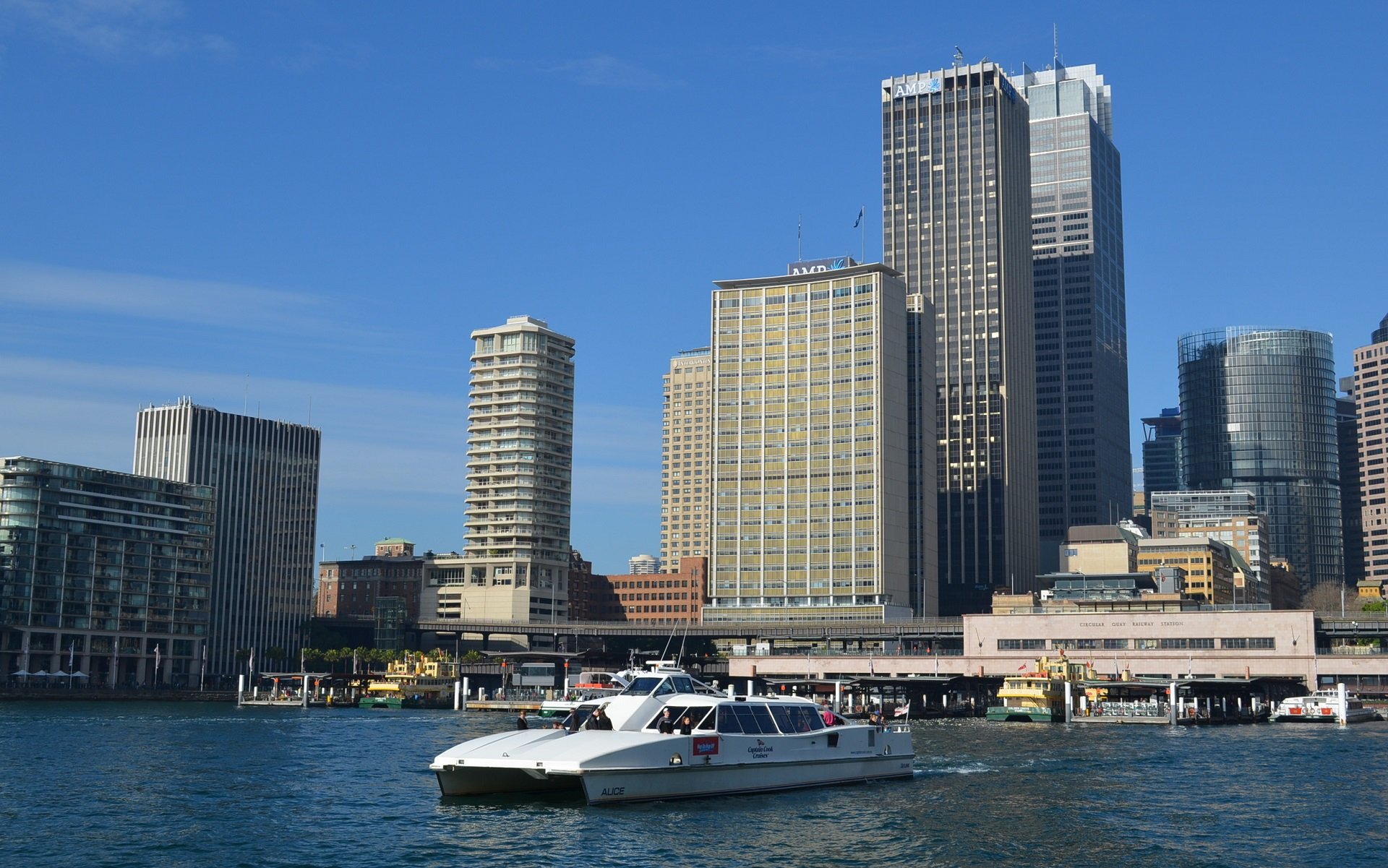 Circular Quay, Sydney cityscape with a ferry at the harbor, skyscrapers in the background, a boat at the wharf, capturing the essence of urban Australia.