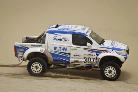 HD PC desktop wallpaper featuring a Toyota Hilux off-road racing vehicle covered in sponsor decals, driving through a sandy terrain.