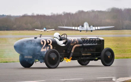 HD desktop wallpaper featuring Ben Collins as The Stig driving the BMW Brutus vintage vehicle on a runway with planes in the background.