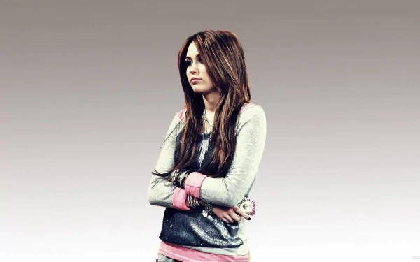 A high-definition desktop wallpaper featuring Miley Cyrus, with her arms crossed and a contemplative expression, set against a gradient background.