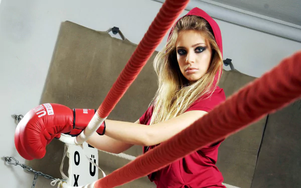 A striking HD desktop wallpaper featuring a woman in a boxing ring, wearing red gloves and a hoodie, exuding strength and determination.