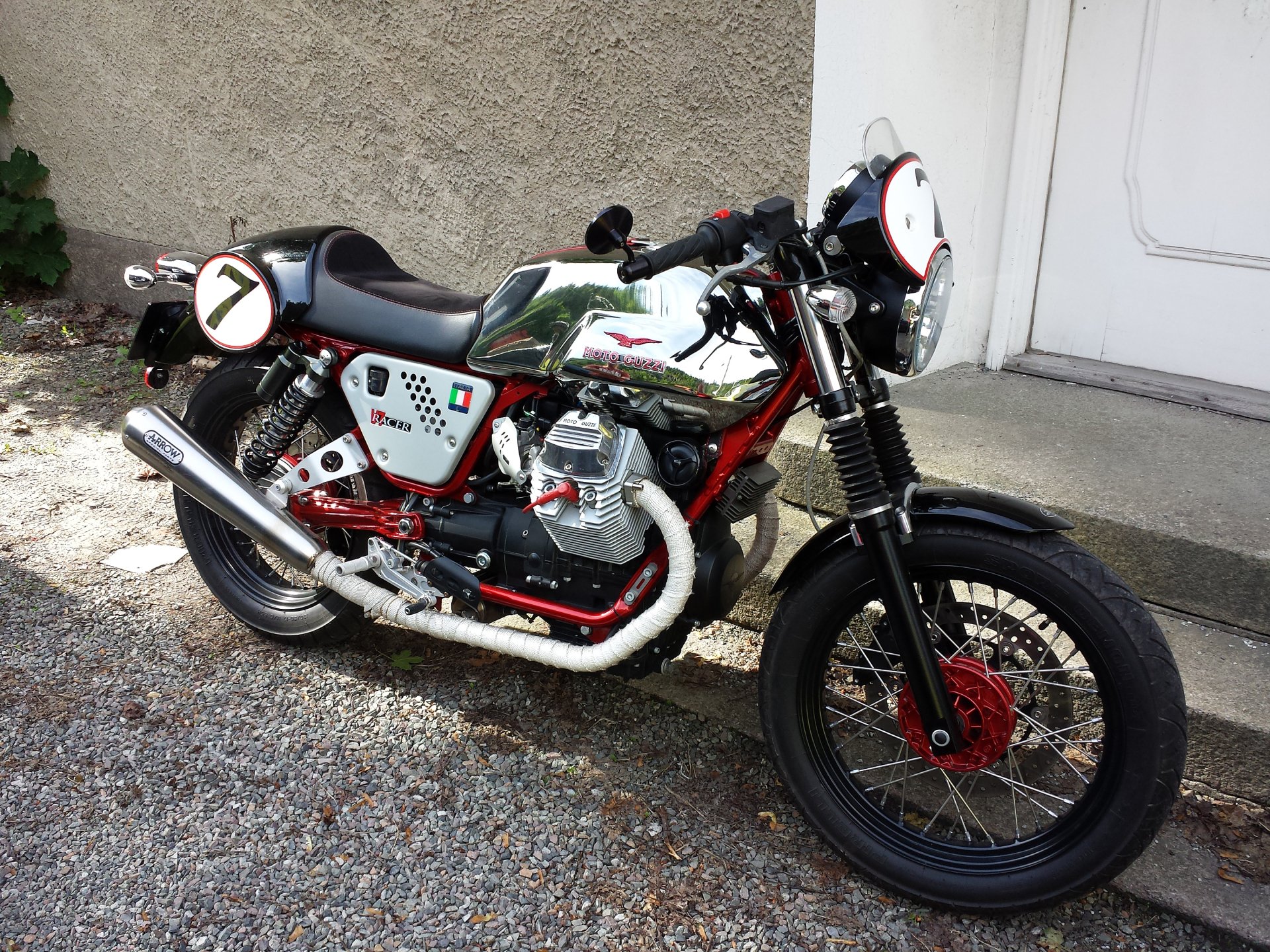 HD desktop wallpaper featuring a classic Moto Guzzi motorcycle parked on a gravel surface near a building wall.