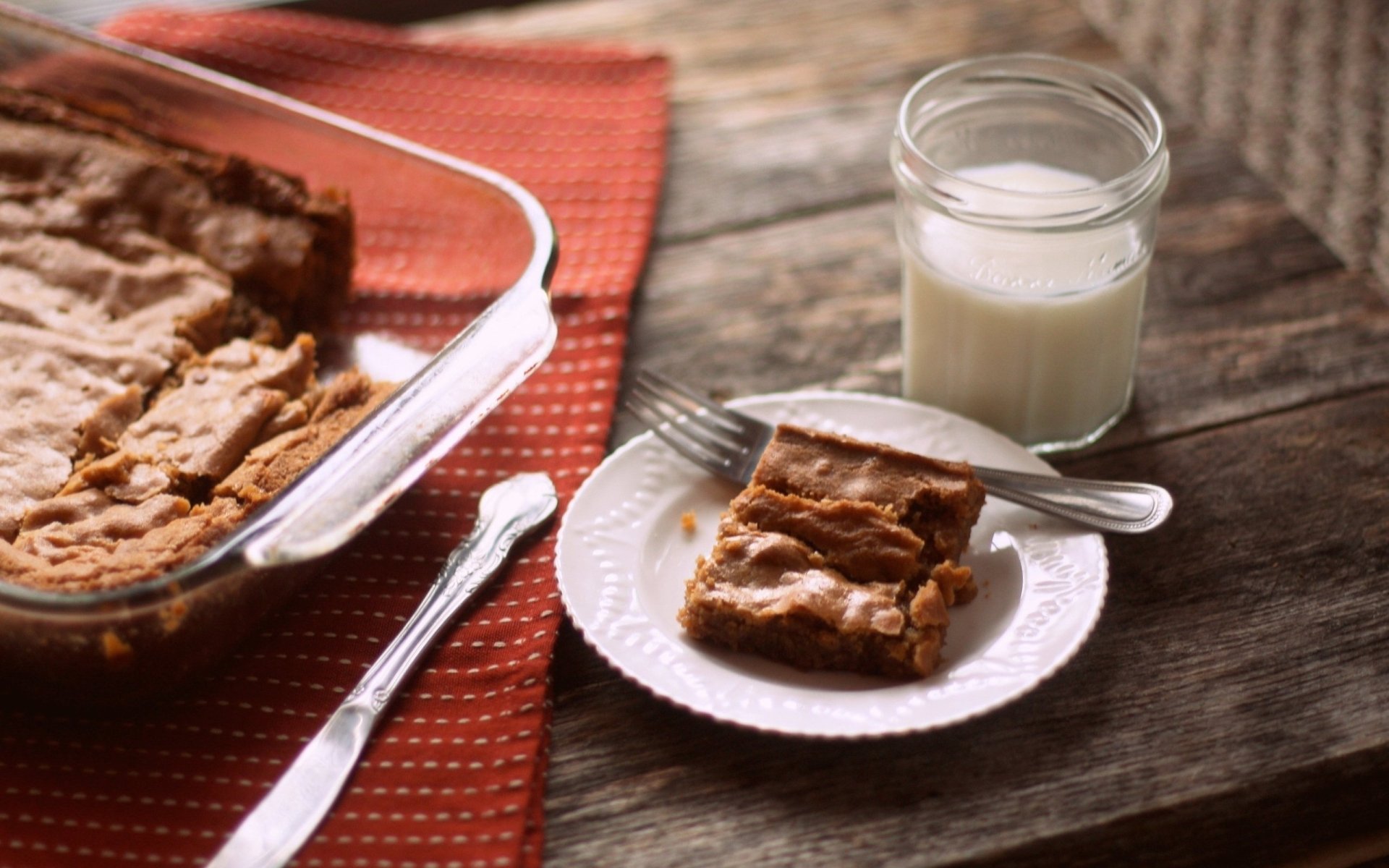HD PC desktop wallpaper featuring a freshly baked dessert square on a plate with a glass of milk, set on a rustic wooden table with baking tools nearby.