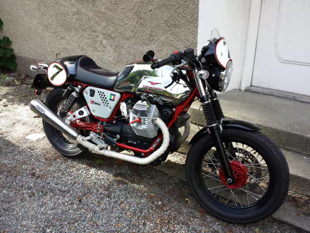 HD desktop wallpaper featuring a classic Moto Guzzi motorcycle parked on a gravel surface near a building wall.