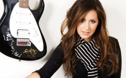 HD desktop wallpaper featuring celebrity Ashley Tisdale posing beside a signed electric guitar, showcasing her stylish look and casual vibe.